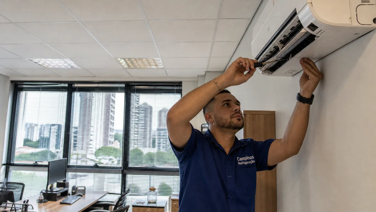 Técnico de uniforme revisando ar-condicionado split em escritório comercial com iluminação natural